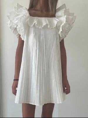 Vit plisserad volangklänning - Supersöt vit kortklänning med plisserat tyg och stora volangdetaljer vid axlarna, från Zara🌟Perfekt till studenten! Första bilden är lånad. Den är helt oanvänd, säljer då jag köpte en annan klänning.