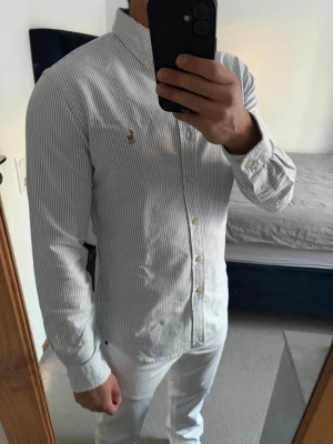 Randig Ralph Lauren skjorta - Klassisk randig skjorta med tunna blå ränder från Ralph Lauren i storlek S. Skjortan har button-down krage och långa ärmar. Ikoniska broderade loggan på bröstet. Perfekt för en clean look samt inför finare tillfällen. Inga defekter! Bara att kontakta vid funderingar!🌟
