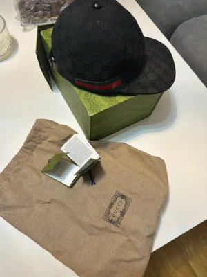 Svart keps  - Snygg svart keps och en grön-röd rand på sidan. Kepsen har böjd skärm och justerbar rem bak. Tillverkad i canvasmaterial 