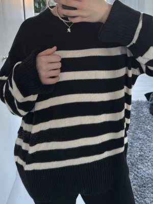 Randig svartvit stickad tröja Gina Tricot - Oversized stickad tröja från Gina Tricot i svart och vitt med breda horisontella ränder. Tröjan har rund halsringning, långa ärmar och ribbade muddar vid ärmslut och nederkant. Perfekt för en avslappnad och trendig look.
