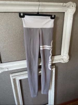 Gråa tights från Aim'n med hög midja - Snygga gråa träningstights från Aim'n med bred vit hög midja och stort vitt tryck längs benet. Tillverkade i stretchigt material.