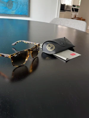 Ray-Ban boyfriend Turtleskal Solglasögon - Säljer ett par Ray-Ban boyfriend solglasögon med klassiskt turtleskal-mönster i brunt och svart. Snygg fyrkantig form och ikonisk logga på bågen. Kommer med originalfodral och putsduk. Perfekta för soliga dagar och trendig look.