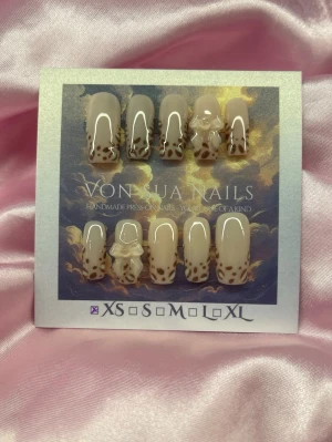 SoftLeo (XS);Medium Square;Curved - Snygga handgjorda press-on naglar i nude beige med brunt leopardmönster och glansig finish. Några naglar har en söt 3D-rosett som detalj. Naglarna är medium långa och har en squareform design. Perfekt för dig som vill ha ett unikt och trendigt nagelset.XS: 14 mm, 11 mm, 11,5 mm, 10 mm, 8 mm 