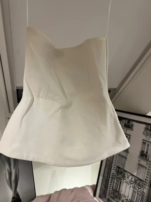 Vit tight tubb topp  - Säljer en stilren vit tighr topp med inga band och figurnära passform. Toppen har en lätt utsvängd nederkant och markerade sömmar framtill för en snygg siluett. Perfekt att styla med jeans eller kjol för en trendig look.