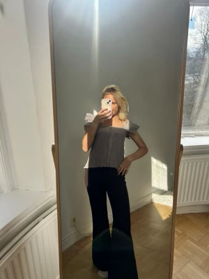 Grå offshoulder blus med volang💖✨ - Trendig grå offshoulder blus med volangdetaljer och knappar framtill. Blusen har korta ärmar och en luftig, croppad passform som ger en avslappnad men ändå stilsäker look. Perfekt att matcha med höga byxor eller kjol.