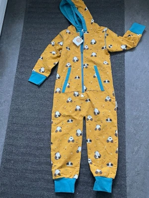 Gul onepiece med pandamönster - Säljer en gul onepiece från Mini Rodini med sött pandamönster och turkosa detaljer. Dragkedja framtill, huva med turkos insida och muddar vid ärmar och benslut. Perfekt för chill dagar hemma eller som mysplagg.