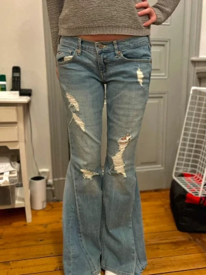 Lågmidjade jeans med slitningar - Säljer dessa lågmidjde jeans som är omsydda till bootcut från hollister. Jeansen har slitningar på benen och har inga fläckar eller andra defekter. Midjemått 38 cm och innerbenslängd 80 cm💞💞