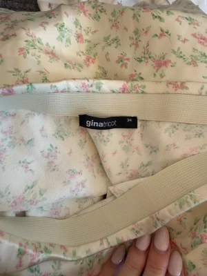 Blommig kortkjol från Gina Tricot - Söt kortkjol från Gina Tricot med blommigt mönster i ljusrosa och grönt på en krämvit botten. Kjolen har en enkel, rak passform och är tillverkad i ett mjukt, lätt material som passar perfekt till varmare dagar.