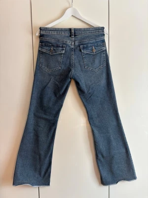 Blå bootcut jeans med fickdetaljer - Säljer ett par blå klassiska bootcut jeans med snygga fickdetaljer samt silverknappar bak. Jeansen har normalhög/låg midja beroende på kroppstyp. Jeansen har också utsvängda ben. Jeansen är i storlek 40 men känns mer som 36-38. Säljer dessa snygga jeans då de inte passar mig, men hoppas de finner en ny garderob!