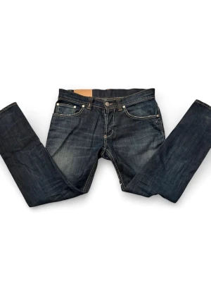 Mörkblå jeans DonDup - Snygga mörkblå jeans ifrån DonDup med raka ben och kontrastsömmar. Klassisk femficksmodell med slitningar framtill för en cool look. Jeansen har detaljerade bakfickor och metallknapp i midjan. Perfekta för dig som gillar en avslappnad men trendig stil.