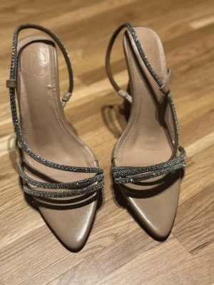 Beige pumps med strassdetaljer - Snygga beige pumps från Balenciaga med tunna remmar dekorerade med glittrande strass. Ena klacken är lite sne dock!