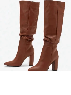 Stövlar bruna  - Snygga bruna stövlar i slouchy modell med hög klack och spetsig tå. Tillverkade i ett läderliknande material som ger en trendig look. Stövlarna går upp till knäna och har en bredare skaftöppning för en avslappnad passform. Aldrig använda 