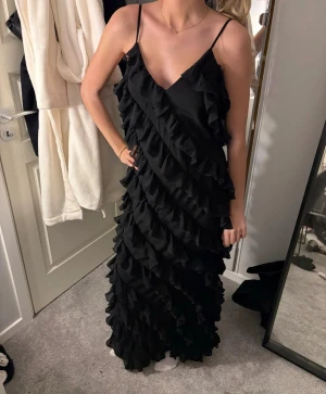 Svart maxiklänning/balklänning - Svart maxiklänning med volanger i storlek 38 från NA-KD. Perfekt till bal eller finare tillfällen. Köpt på Vinted så säljer i andrahand. Säljer då jag har hittat en annan. Aldrig använd av mig, men använd en gång på bal av en tidigare ägare. (Min vän på bilden är 172cm) pris kan absolut diskuteras, skriv vid frågor.💕