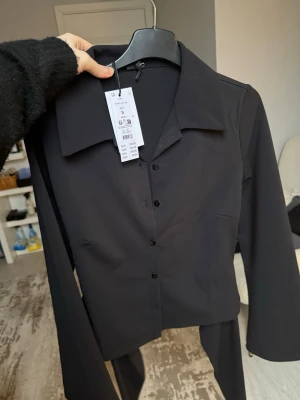 Tie back collar top från Gina Tricot - Trendig svart skjorta från Gina Tricot med figurnära passform och långa ärmar. Skjortan har klassisk krage, knäppning framtill och är tillverkad i ett mjukt material som ger en snygg siluett. Perfekt till jeans eller kjol för en clean look.