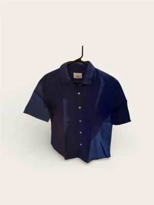 Bläck Linneskjorta (Kortärmad) – Marinblå (Strl XS) - Säljer en stilren kortärmad skjorta från Bläck (MQ). Perfekt basplagg inför sommaren eller utlandsresan. Tillverkad i svalt linnematerial (eller linneblend) som andas. Färgen är en klassisk mörkblå som passar lika bra till jeans som till beigea shorts.  Skick: Mycket fint skick! Inga fläckar eller slitningar. Hel och ren.  Storlek: Extra Small (XS). (Passar dig som är smalare eller junior).