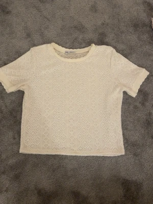 Vit spetsmönstrad topp från Zara - Söt vit topp från Zara med korta ärmar och spetsmönster i hela tyget. Toppen har rund halsringning och vågiga kanter vid ärmslut och nederkant. Perfekt för dig som gillar romantisk och feminin stil.