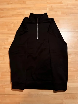 Half zip hoodie - En stilren svart hoodie med half zip dragkedja framtill och hög krage. Ribbade muddar vid ärmslut och nederkant. Perfekt för en avslappnad och trendig look.