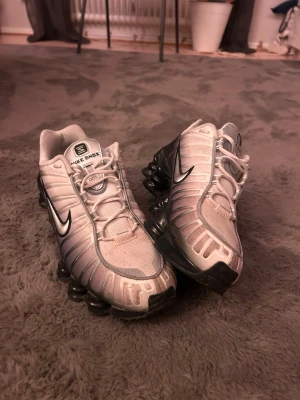 Nike Shox vita och svarta sneakers - Nike Shox sneakers i vitt och svart med ikoniska fjädrande sulor. Skorna har en futuristisk design med mesh och syntetmaterial, svarta detaljer och silverfärgad Swoosh på sidan. Perfekta för dig som vill sticka ut med en sportig och modern look. använda ett par gånger men i super skick
