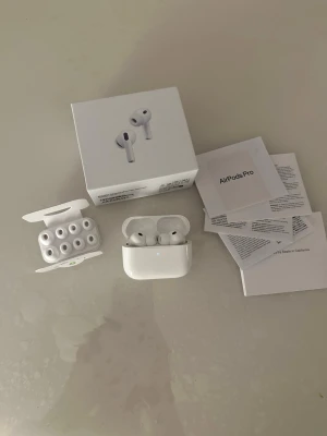 Apple AirPods Pro 3 - Säljer ett par vita Apple AirPods Pro med laddningsetui och flera utbytbara silikonpluggar. Hörlurarna har en stilren och kompakt design i blank plast och levereras med originalförpackning och manualer. Perfekta för dig som vill ha grymt ljud och smidig anslutning.