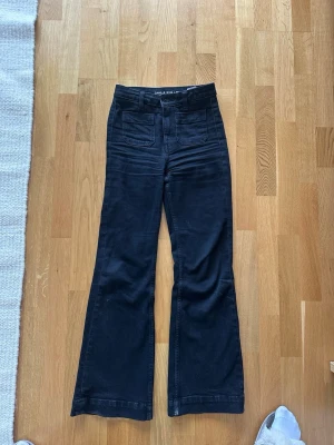 Svarta utsvängda jeans Camille - Snygga svarta jeans med hög midja och utsvängda ben. Jeansen har två stora fickor framtill och bälteshällor. Perfekta för en trendig och avslappnad stil.