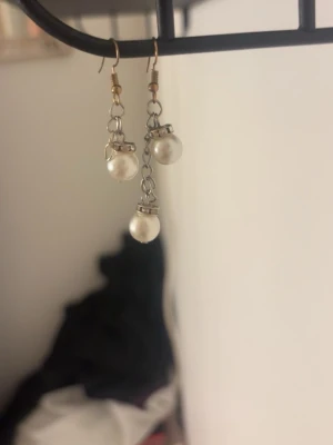 Silvriga örhängen med vita pärlor - Säljer ett par snygga örhängen med dubbla vita pärlor i droppform, fästa på silverfärgade kedjor. Örhängena har metallkrokar och en stilren design som passar till många olika looks. Perfekta för dig som gillar klassiska accessoarer med en twist. jag har gjort de hemma själv så snabbt köp’