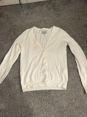 Vit kofta från Anna Field - Klassisk vit kofta från Anna Field med v-ringning och knäppning framtill. Långärmad modell i tunt, mjukt material som passar perfekt till lager på lager. Enkel och stilren design som funkar till det mesta.