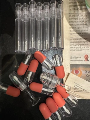 Tomma läppglanshylsor med röd kork - Säljer flera tomma läppglanshylsor i transparent plast med mattröd kork och applikator. Perfekt för dig som vill skapa eget läppglans eller fylla på favoritprodukten. Snygg och modern design med rundad form och tydlig applikator.