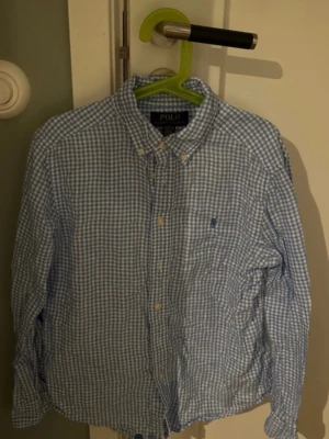 Blårutig skjorta från Polo Ralph Lauren storlek 10-12 år 152 - Klassisk blårutig skjorta från Polo Ralph Lauren med button-down krage och broderad logga på bröstet. Skjortan har långa ärmar och knäppning framtill. Perfekt för en clean och stilren look.