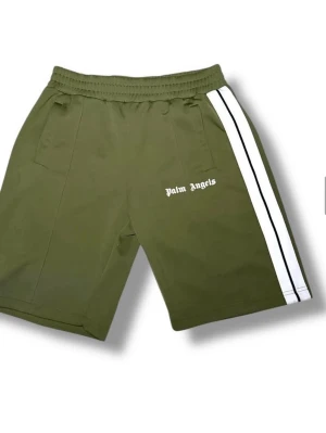 Palm Angels gröna shorts med ränder - Snygga olivgröna shorts från Palm Angels med vita dubbla ränder längs sidorna och logga tryckt på vänster ben. Shortsen har elastisk midja och sidofickor, perfekta för en avslappnad streetwear-look.