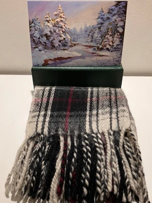 Varm  ullhalsduk med fransar - Snygg halsduk i klassiskt rutigt mönster med svart, vitt, grått och röda detaljer. Halsduken är stickad i mjuk ull och har grova tvinnade fransar i ändarna. Perfekt accessoar för att hålla värmen och lyfta din outfit.