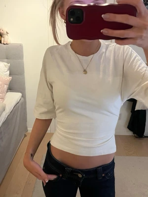 Vit croppad topp med knyt i ryggen från Nelly - Säljer en vit croppad topp med halvlånga ärmar och snygg knytning i ryggen. Toppen har en tight passform och är tillverkad i mjuk bomull. Perfekt för dig som gillar trendiga och stilrena plagg.