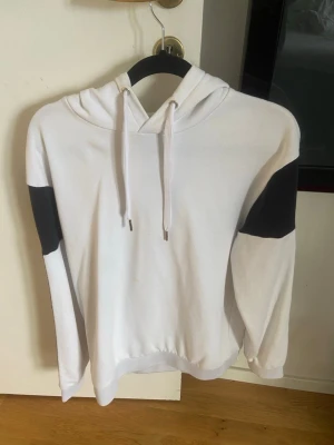 Vit Armani hoodie  - Snygg vit hoodie med svarta partier på ärmarna och justerbar dragsko i huvan. Klassisk passform och ribbade muddar vid ärmslut och nederkant. Perfekt för en avslappnad streetstyle-look. Pris är förhandlingsbart 