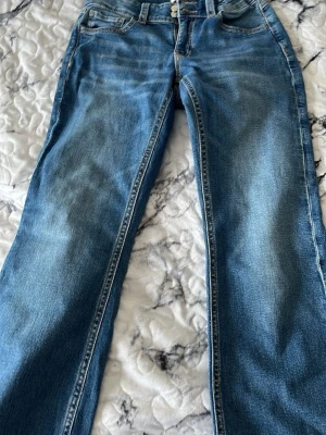 Blå raka jeans med ljus tvätt - Säljer ett par klassiska blå jeans med rak passform och ljus tvätt. Jeansen har fem fickor, bälteshällor och stängs med knapp och dragkedja. Materialet är denim i bomull och sömmarna är i kontrastfärg. Perfekta till en avslappnad stil.