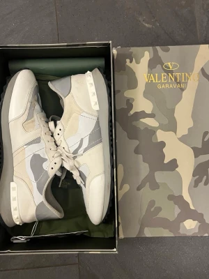 Valentino rockrunners - Snygga sneakers från Valentino Garavani i beige, vitt och grått med camomönster. Skorna har coola nitar på hälen, vita snören och en mix av läder och textil. Perfekta för dig som vill sticka ut med exklusiv streetstyle.