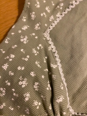 Grön blommig topp från H&M Divided - Söt ljusgrön topp från H&M Divided med små vita blommor och ribbad struktur. Toppen har spetsdetalj längs kanten och är perfekt för en trendig och avslappnad look.