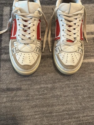 Valentino vita och röda sneakers - Snygga vita sneakers från Valentino med röda detaljer och stort VLTN-tryck på sidan. Skorna har perforerad tå, vita snören och en chunky sula. Tillverkade i läder och textil för en exklusiv känsla och cool look.