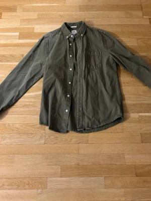 Olivgrön skjorta från Zara - Stilren olivgrön skjorta från Zara med klassisk krage och bröstficka. Skjortan har långa ärmar och knappar framtill. Perfekt för en avslappnad men snygg look.