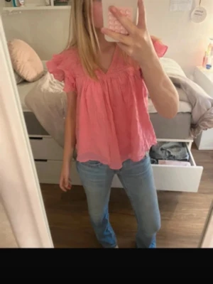 Rosa volangblus med kort ärm - Supersöt rosa blus med volangdetaljer och korta ärmar. Luftig och flowy modell med v-ringning, perfekt för varmare dagar. Passar snyggt till både jeans och kjol. Ingen synlig logga eller märke. Storlek 158/164