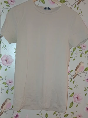 Beige basic t-shirt i bomull - Enkel och stilren beige t-shirt med rund hals och korta ärmar. Tillverkad i mjukt bomullstyg som känns skönt mot huden. Perfekt att matcha med jeans eller shorts för en avslappnad look.