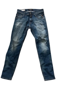 Blå Replay jeans med slitningar - Säljer ett par snygga blå jeans från Replay i modellen 28/30. Jeansen har coola slitningar och tvättade detaljer för en trendig look. Tillverkade i ekologisk bomull och har klassisk femficksdesign med dragkedjegylf.