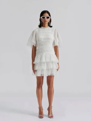 Oanvänd MINNIE MINIKLÄNNING By Malina  - Superfin vit kort klänning från By Malina med flera lager volanger och otroligt snygg överdel. Klänningen har korta, vida ärmar och är tillverkad i ett lätt, transparent tyg med struktur. Perfekt för dig som vill ha en sjukt snygg klänning på studenten!