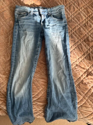 Blå bootcut jeans från Gina Tricot - Snygga blå bootcut jeans från Gina Tricot med klassisk femficksdesign och ljusa slitningar framtill. Jeansen har låg midja och är tillverkade i mjukt denimtyg. Perfekta för en avslappnad och trendig look. Jag har sprättat de där nere men de e fint gjort