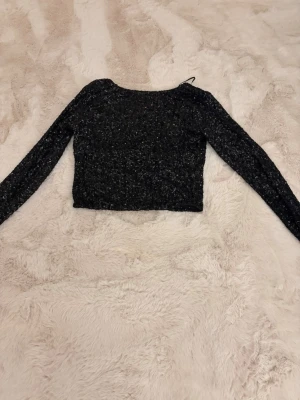 Svart glittrig croppad topp - Snygg svart croppad topp med paljetter med långa ärmar i storlek L men passar även för dem med M i storlek. Toppen är figurnära i modellen. Oanvänd. 