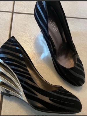 Svarta pumps med metallicklack - Unika svarta pumps från Xardi London med zebramönstrade ränder i sammet och en cool metallicklack i silver. Skorna har spetsig tå och låg klack, perfekta för dig som vill sticka ut med din stil.