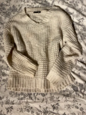 Beige stickad tröja med v-ringning - Mysig beige stickad tröja från lager med v-ringad hals och grovstickat mönster. Tröjan har långa ärmar och breda ribbade muddar vid ärmslut och nederkant. Perfekt för lager-på-lager och en avslappnad stil.