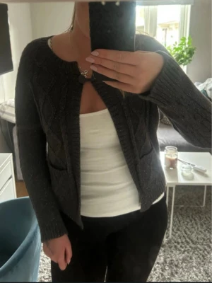 Mörkgrå stickad kofta från Gina Tricot - Mysig mörkgrå stickad kofta från H&M med dekorativa diamantmönster och två fickor framtill. Koftan har rund halsringning, ribbade muddar och stängs med en knapp upptill. Perfekt att slänga över en topp för en snygg lager-på-lager-look.