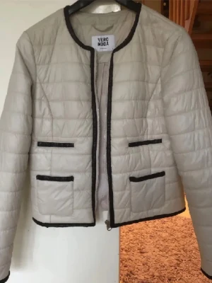jacka från Vero Moda - PRIS KAN DISKUTERAS!! Stilren beige quiltad jacka från Vero Moda med svarta kontrastkanter och fyra dekorativa fickor framtill. Jackan har rund halsringning och är tillverkad i ett lätt, vadderat material som ger en trendig look.