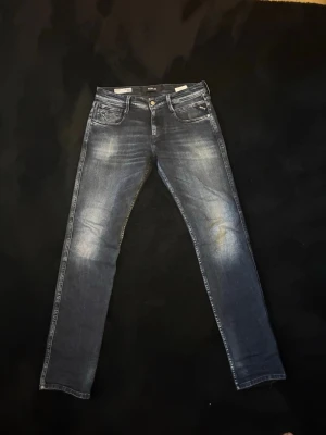 Mörkblå slim fit jeans från Replay - Snygga mörkblå slim fit jeans från Replay med slitna detaljer och klassisk femficksdesign. Jeansen har en tvättad look med ljusare partier på lår och knän, samt normal midja. Perfekta för en trendig och avslappnad stil.