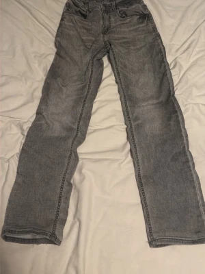 Grå jeans - Grå jeans med rak passform och klassisk femficksdesign. Jeansen har en tvättad look och är tillverkade i denim, vilket ger en avslappnad och trendig vibe. Perfekta för dig som gillar en stilren och enkel look.