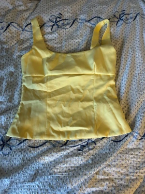 Gul linnetopp med rosett - Snygg gul linnetopp med breda axelband och en stor rosett i ryggen. Toppen har en figurnära passform och är tillverkad i ett slätt tyg som känns som bomull eller polyester. Perfekt för dig som vill sticka ut med en färgglad och trendig look. Liknande topper från Zara!💓